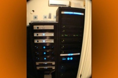 Two equipment racks with lit front panels in an equipment room with its own wall-mounted air conditioner