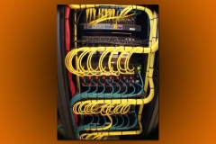 Back of an equipment rack with yellow and teal cables looped and tied in even rows