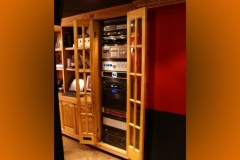 Equipment rack built into a wood cabinet with glass-paned doors, beside bookshelves
