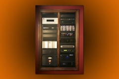 Equipment rack built into the wall behind a wood frame, two bays of components and a shelf of discs