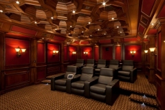Home theater with an octagonal coffered wood ceiling, red paneled walls with sconces and tiered rows of leather recliners