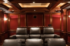 Rear of a home theater: leather recliners in front of a bar-height counter, red paneling and a lit coffered ceiling