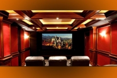 Home theater with red fabric wall panels between wood pilasters, a coffered ceiling and three leather recliners