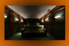 Home theater with dark green fabric walls, wood pilasters, sconces and two rows of leather seating