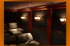 Home theater with dark green fabric walls, wood pilasters, alabaster sconces and leather recliners