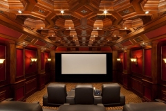 Home theater with an octagonal coffered wood ceiling, red wall panels, sconces and leather recliners facing the screen