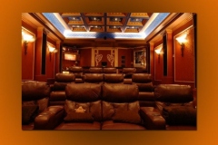 Home theater seen from the screen: three tiered rows of leather recliners, sconces and a lit coffered ceiling