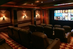 Home theater with red checkered carpet, three rows of leather recliners and sconces on paneled walls
