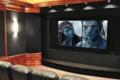 Home theater with black fabric walls, a framed screen, cherry wood wainscot and a wall sconce