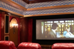 Screen wall of a home theater with red drapes, arched niches with sconces and a lattice-painted ceiling
