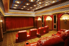 Home theater with tiered red leather recliners, a red stage curtain, arched niches with sconces and a coffered ceiling