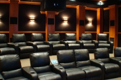 Home theater with three rows of black leather recliners, wood columns, black fabric walls and wall sconces