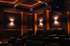 Rows of black leather recliners under a cove-lit coffered ceiling, with wood columns and slotted sconces