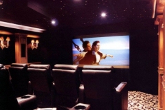 Home theater with a star ceiling, sconces on wood paneling and rows of black leather recliners