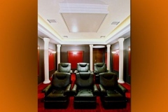 Home theater with white columns, red wall panels, a tray ceiling and two rows of black leather recliners