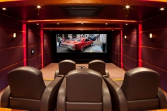 View from behind leather recliners toward the screen, framed by red LED strips on padded walls