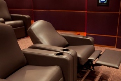 Close-up of brown leather theater recliners with cup holders, one with its footrest raised
