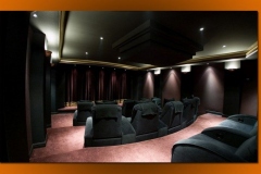 Home theater with curved rows of dark fabric recliners on tiered carpeted platforms and a curtained front wall