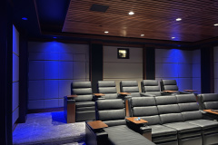 Modern home theater with a slatted wood ceiling, blue accent lighting, padded walls and gray leather seating
