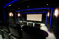 Home theater with blue LED outlines on the soffits and walls, black leather recliners and a white screen