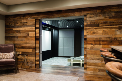 Home theater seen through a doorway in a reclaimed barnwood wall, beside a bar and armchair