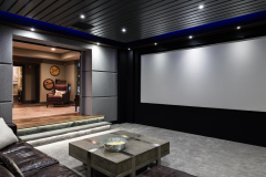 Modern home theater with a large screen, gray padded walls and an open doorway to a lounge with lit steps