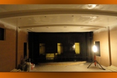 Theater shell with a curved ceiling soffit, black front wall with three openings for speakers, and work lights
