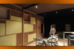 Wall frames being built out with yellow insulation in the bays, black ceiling and recessed lights