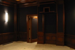 Theater wall with dark fabric panels and wood wainscot being installed around the door