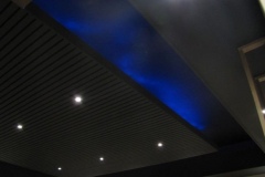 Theater ceiling under construction: slatted black panels, recessed lights and a blue-lit cove
