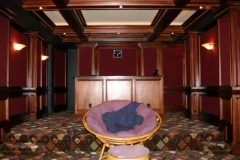 Theater with wood paneling and columns, red fabric wall panels, sconces and a tiered carpeted floor