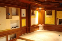 Wood-paneled theater with wall bays still open: yellow insulation, wiring and electrical boxes