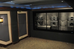 Theater with the screen wall open, showing front speakers and subwoofers on a quilted black backing