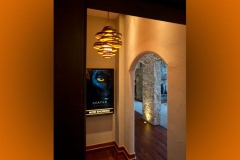 Hallway to the theater with a lit "Now Showing" poster box, spiral pendant and stone arch beyond