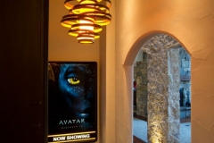 Lit "Now Showing" movie poster beside an arched stone opening and spiral pendant light