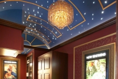 Starry blue lobby ceiling with gilded trim and crystal chandelier above lit poster cases