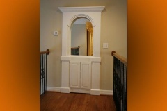 White arched millwork surround with a paneled cabinet below, on a stair landing