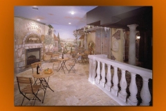 Italian street-café themed lobby with a painted mural, bistro tables and a stone balustrade