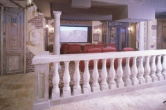 Stone balustrade overlooking a home theater with red seats, under an Italian village mural