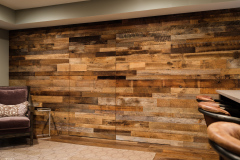 Reclaimed barnwood wall with the outline of a flush door set into it, beside a bar and armchair