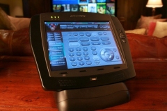 Crestron touch-panel remote on a table, its screen showing buttons to watch a movie or play music