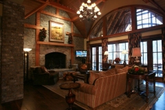 Great room with a stone fireplace, timber-framed vaulted ceiling, arched windows and a small screen beside the hearth