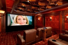 Side view of the screening room: large screen, two rows of leather recliners and a pedestal-mounted touch-panel control